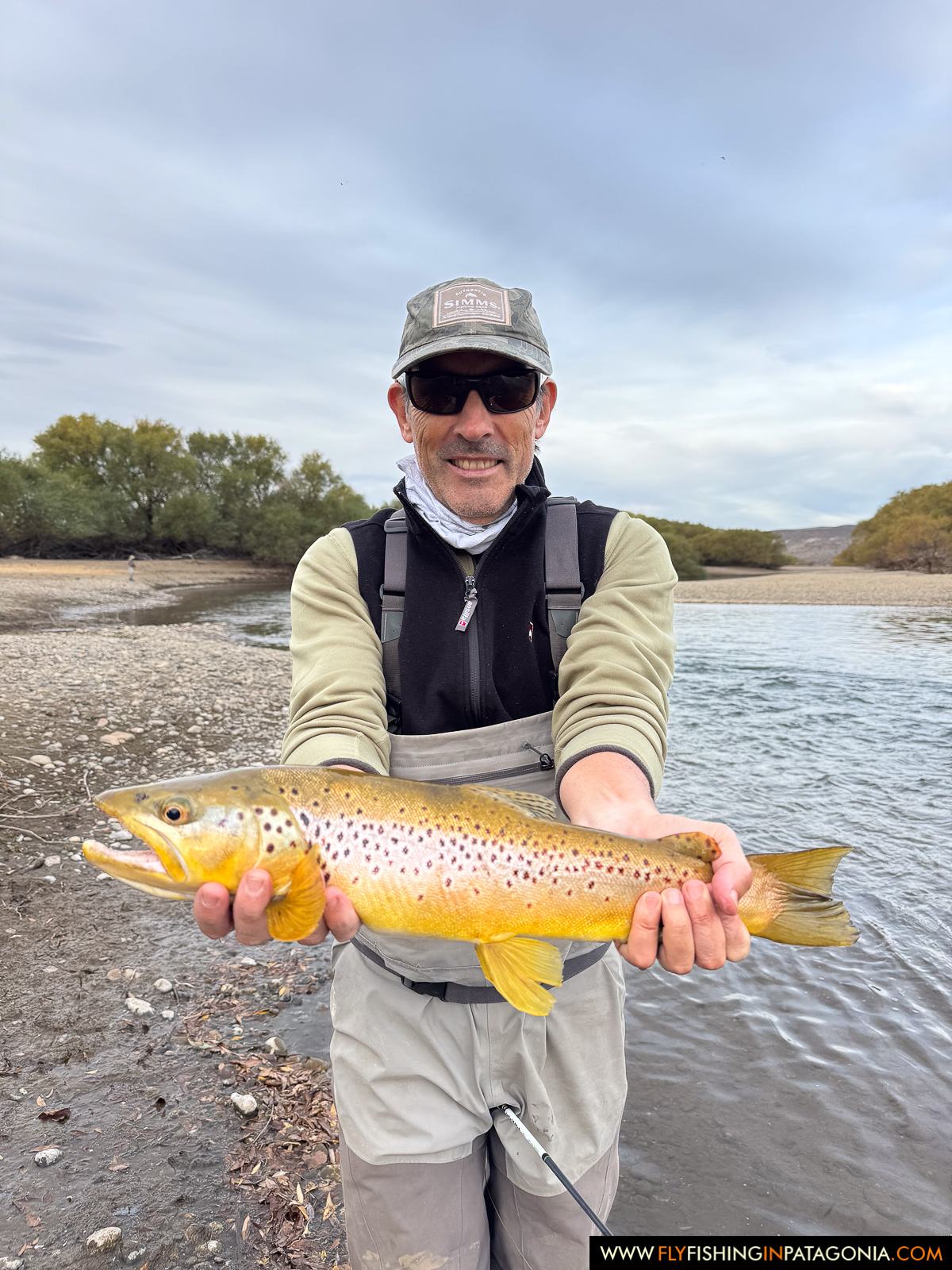 Angler holding a brown trout on a gravel bank of the Collon Cura River
