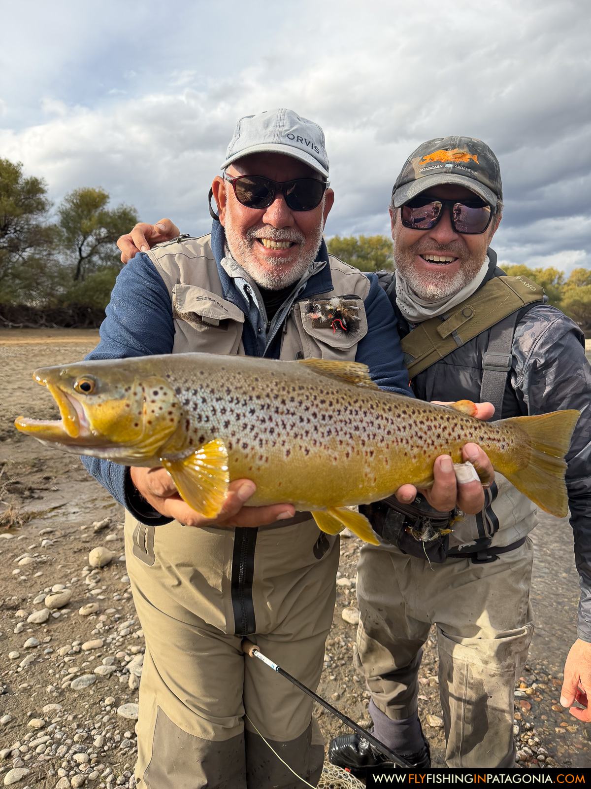 Two anglers holding a brown trout on a Collon Cura River gravel bank