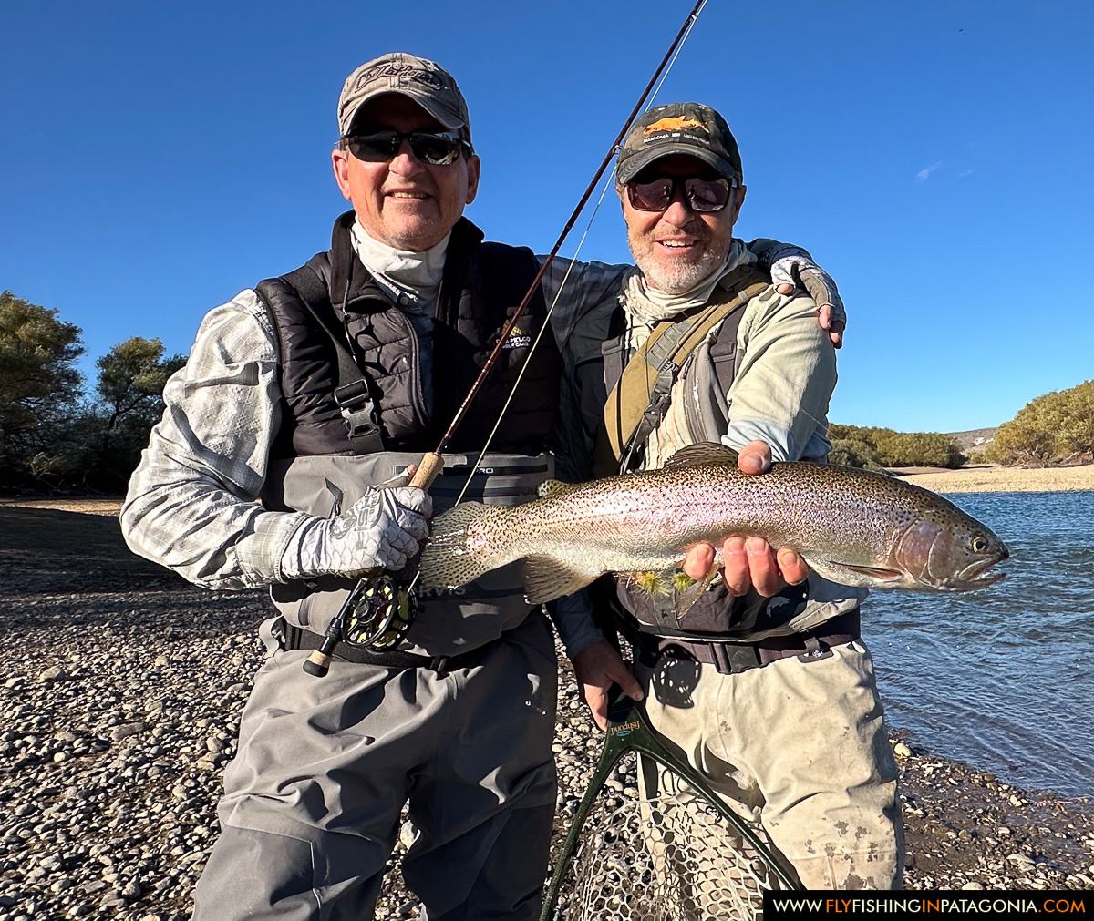 Two anglers holding a brown trout on a gravel bank of the Collon Cura River