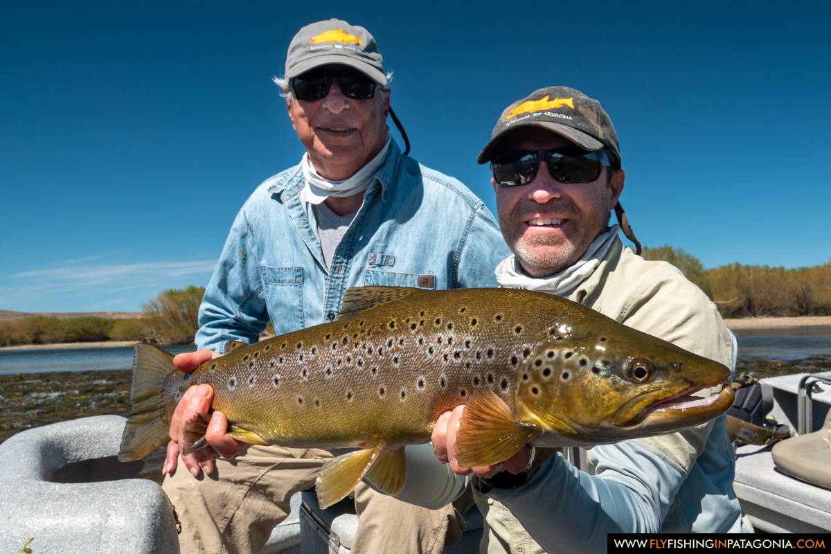Two anglers holding a large brown trout aboard a Collon Cura River drift boat