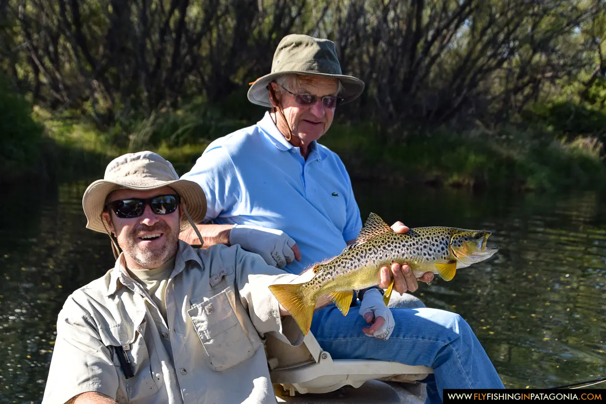 Two anglers holding a brown trout aboard a boat on the Collon Cura River