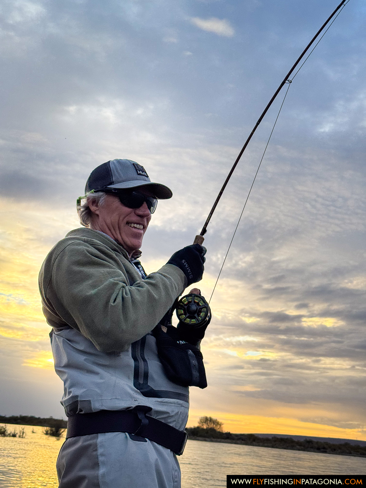 an angler fighting a fish under a golden sunset sky on the middle limay river