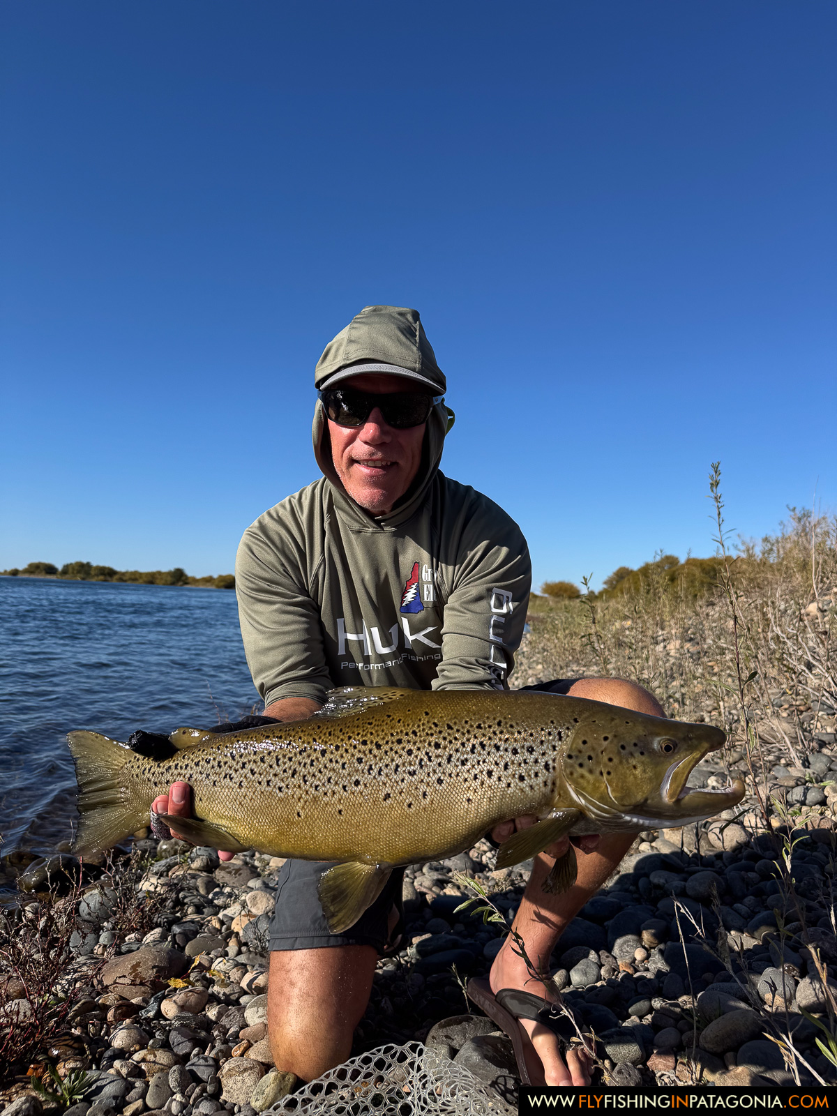 kneeling with a heavy brown trout on the rocky banks of the middle limay river
