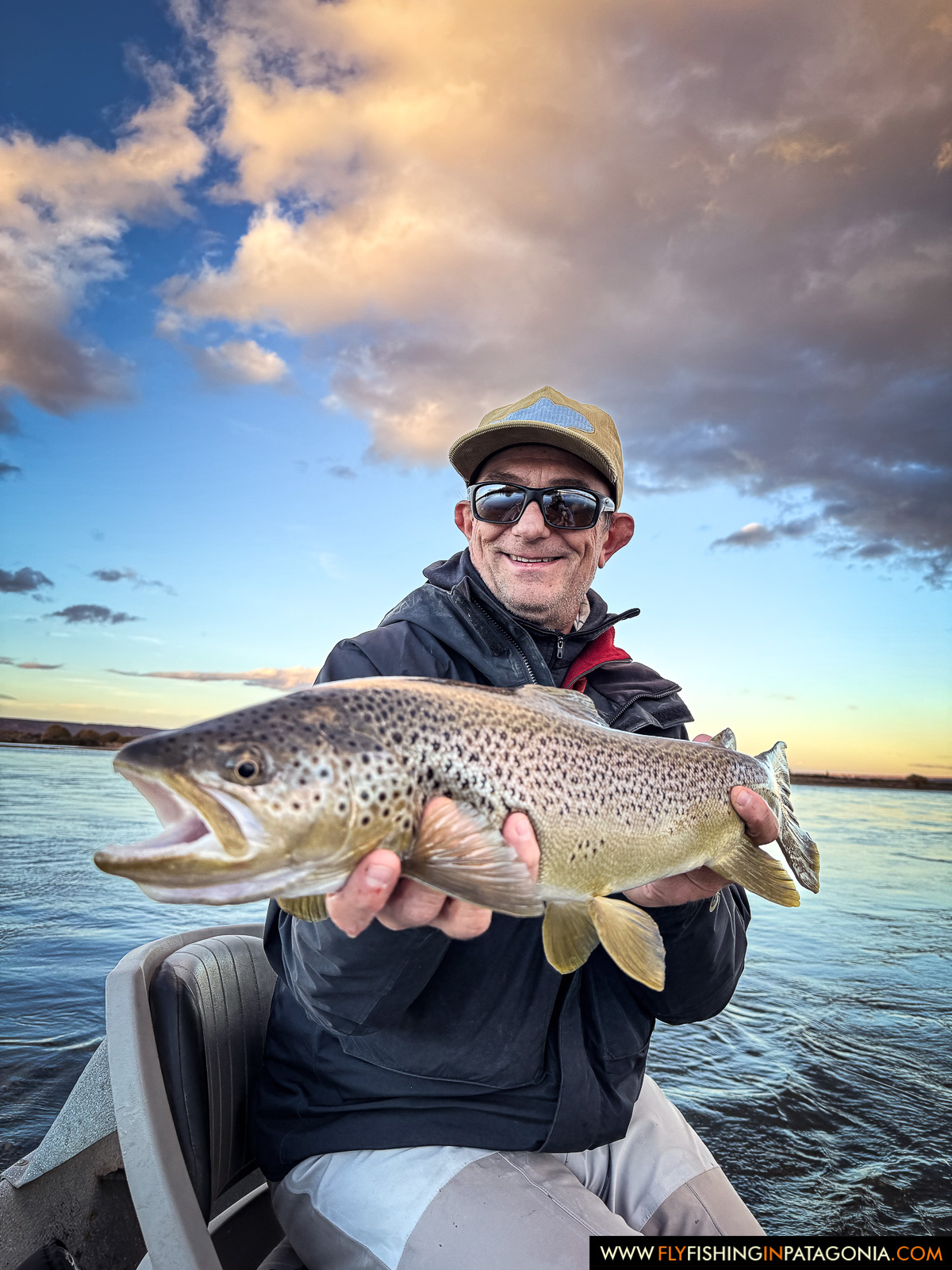 a smiling angler with a great brown trout under the sunset sky on the middle limay river