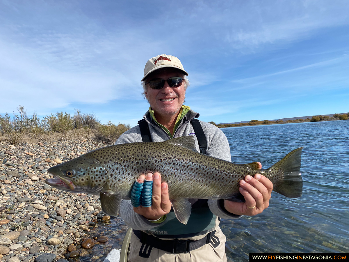 a proud angler with a colorful rainbow trout on the rocky shore of the middle limay river