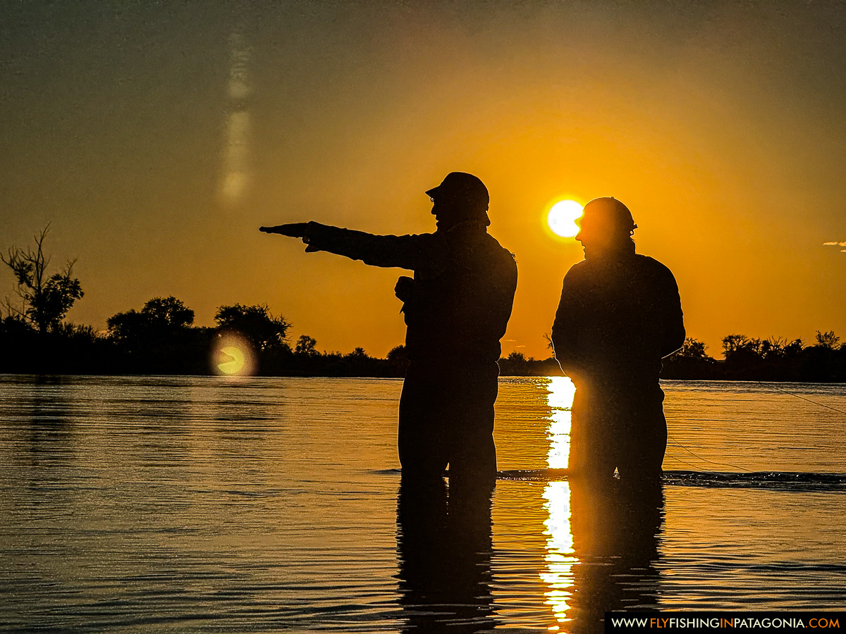two anglers silhouetted against a golden sunset wade fishing the middle limay river