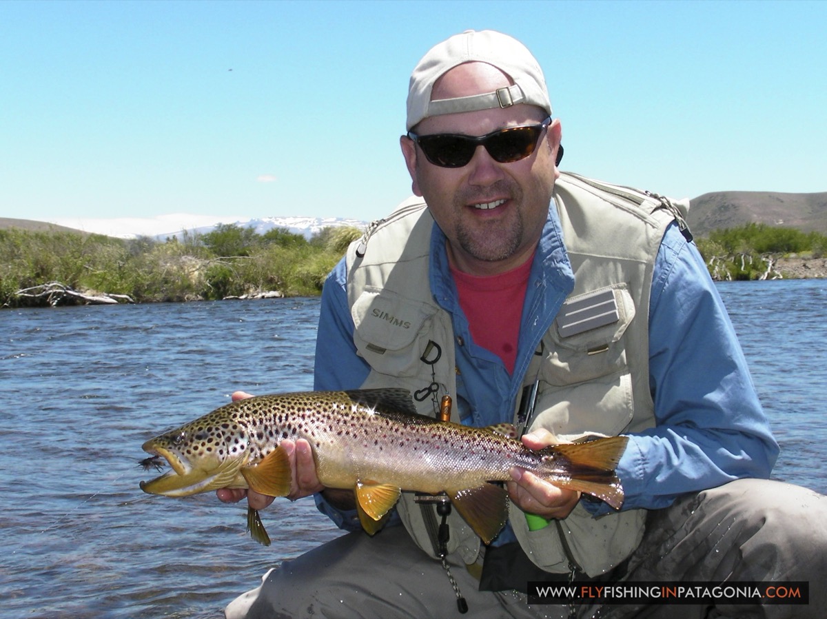 Angler holding a brown trout with snow-capped mountains in the distance