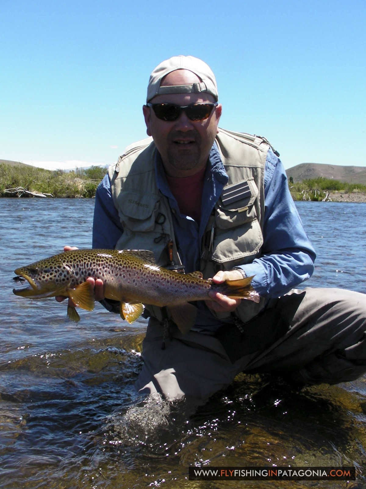 Angler holding a brown trout under a blue sky on the Quemquemtreu stream