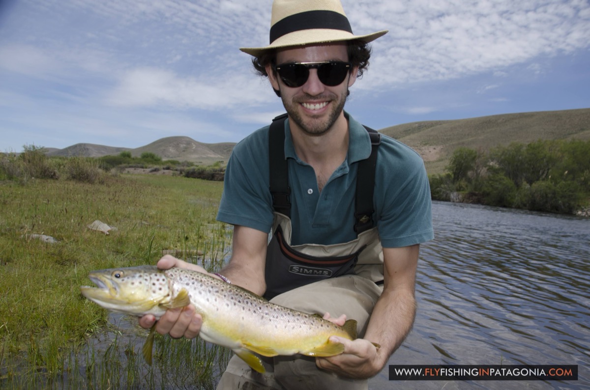 Young angler holding a brown trout beside a grassy bank of the Quemquemtreu stream